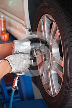car mechanic screwing or unscrewing car wheel of lifted automobi