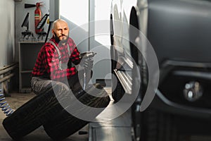 Car mechanic screwing or unscrewing car wheel of lifted automobile by pneumatic wrench at repair service station