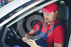 Car mechanic sitting inside the car and writing inspection documents on clipboard