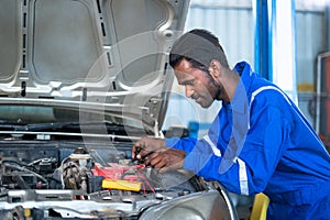 Car mechanic testing or checking car engine battery by using digital multimeter at garage - concept of technology