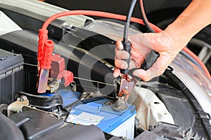 Car mechanic uses battery jumper cables charge a dead battery.