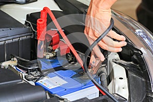 Car mechanic uses battery jumper cables charge a dead battery. photo