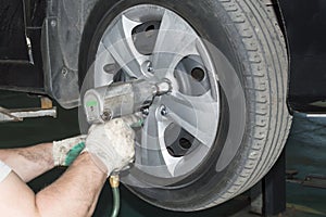 The car mechanic uses a pneumatic wrench to tighten the wheel nut