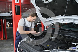 car mechanic using digital tablet with service and maintenance app on screen while inspecting vehicle in auto repair