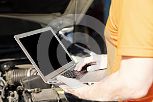 A car mechanic is using a laptop computer to check the engine operation