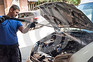 Car mechanic washes the car engine with pressurized water photo