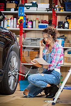 Car mechanic woman in blue overalls talking on the phone near a