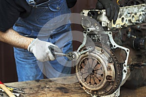 Car mechanic in work gloves unscrews the clutch from the engine block during repair in the workshop.