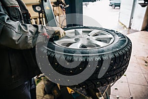 Car mechanic worker doing tire replacement and wheel balancing with special equipment in repair service station