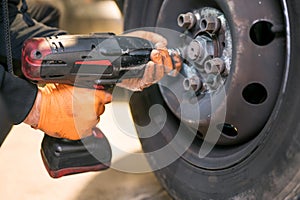 Car mechanic worker doing tire or wheel replacement with electric wrench in garage of repair service station