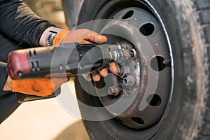 Car mechanic worker doing tire or wheel replacement with electric wrench in garage of repair service station