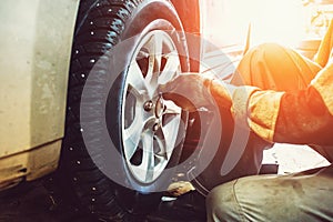 Car mechanic worker doing tire or wheel replacement in garage of repair service station