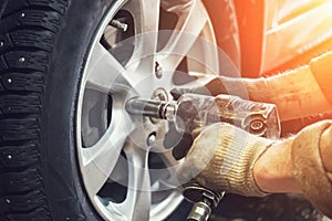 Car mechanic worker doing tire or wheel replacement with pneumatic wrench in garage of repair service station