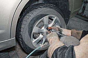 Car mechanic worker doing tire or wheel replacement with pneumatic wrench in garage of repair service station