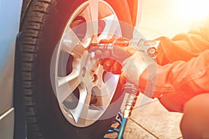 Car mechanic worker doing tire or wheel replacement with pneumatic wrench in garage of repair service station, sunlight effect