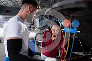 Car mechanic working in an auto repair shop explain to customer after inspecting the operation