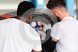 Car mechanic working in an auto repair shop, inspecting the operation of the car's air conditioner