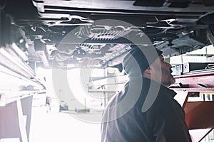 CAUCASIAN MECHANIC CHECKING THE UNDERCARRIAGE OF A CAR DURING A TUNE-UP photo