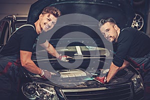 Car mechanics checking under hood in auto repair service.