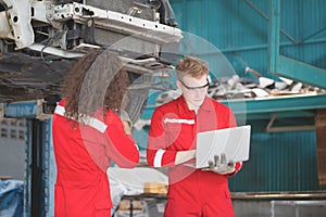 Car mechanics team in uniform are working in auto service with lifted vehicles. Car repair and maintenance