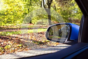 Car mirror Closeup with beautiful autumn landscape in reflection, on the road with the car on empty road blurred background