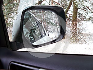 Car mirror. Forest in rear view mirror closeup. Reflected in a rearview. In the background forest. Winter