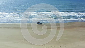 The car moves on a summer day along the sandy sea beach, crosses the rivers and white foam from the waves. Tourists