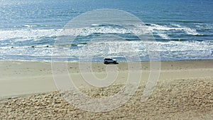 The car moves on a summer day along the sandy sea beach, crosses the rivers and white foam from the waves. Tourists