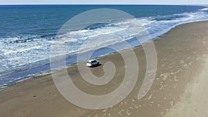 The car moves on a summer day along the sandy sea beach, crosses the rivers and white foam from the waves. Tourists
