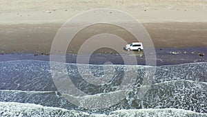 The car moves on a summer day along the sandy sea beach, crosses the rivers and white foam from the waves. Tourists