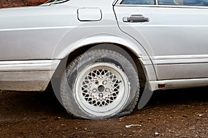 Car with one black flat tire on a white car on gray asphalt