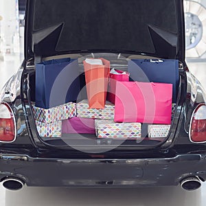 A car with an open trunk is filled with shopping bags. Advertising installation in a shopping center. Holiday shopping.