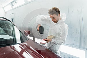 Car painter man determines the correct tone of a vehicle body colour using a special colorist`s lamp.