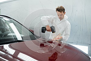 Car painter man determines the correct tone of a vehicle body colour using a special colorist`s lamp.