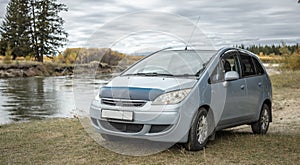 Car is parked on the bank of a river next to a yellow green autumn forest. Concept of beautiful nature and autumn mood