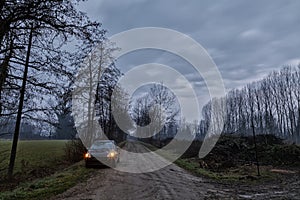 Car parked in the country road with cloudy sky and silhouettes of trees. Night photography.
