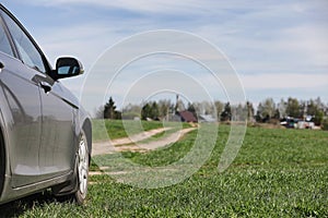 The car is parked in the field. The car is driving along the rural road to the house. The car is gray in the meadow in front of