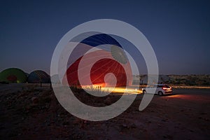 A car parked in front of a hot air balloon with headlights on during night, preparation of a flight in Goreme national park in