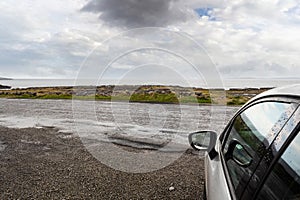 Car parked off road view view on field and clouds over ocean. Wet road. Outdoors activity concpet