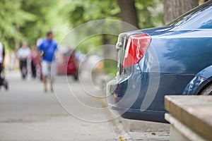 Car parked in pedestrian zone under trees on city street with walking people on summer day