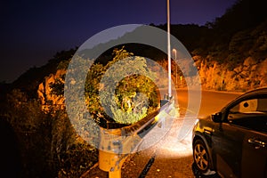 Car parked at the side of a road in the mountains during night time with headlights