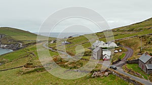 Car passing around houses in countryside. Narrow coastal road between green pastures above sea. Ireland