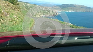 Car point of view of driving on a winding ocean road with descending hill