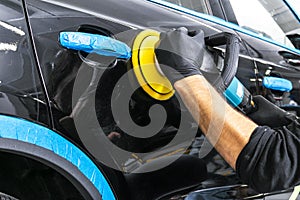 Car polish wax worker hands applying protective tape before polishing. Buffing and polishing car. Car detailing. Man holds a polis