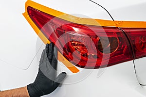 Car polish wax worker hands applying protective tape on the rear lights before polishing. Buffing and polishing car headlight. Car