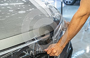 Car protection film or PPF process of wrapping and installing on car hood by detailer worker hands, close up