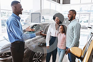 Car purchase or rental. Millennial black family with kid speaking to salesman about buying new automobile at dealership