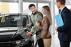 Car purchase or rental. Millennial Caucasian couple speaking to salesman about buying new automobile at dealership