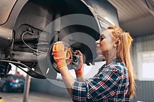 Car reapir. Young red-headed girl, auto mechanic working at auto service station using different work tools. Gender