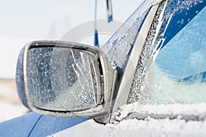 Car rearview mirror covered with white frost and snow on a sunny winter day